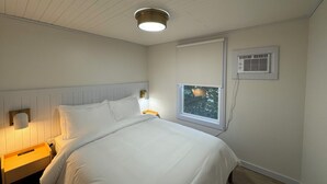 Ein Schlafzimmer mit einem Bett, einem Nachttisch, einer Wandlampe, einem Fenster mit Ausblick und einer Klimaanlage.