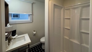 Ein Badezimmer mit Waschbecken, Toilette, Dusche und einem Fenster mit Jalousien.