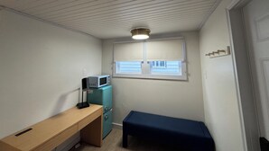 Ein kleines Zimmer mit einem Holztisch, einer blauen Bank, einem türkisfarbenen Kühlschrank, einer Mikrowelle und einem Fenster mit Jalousien.
