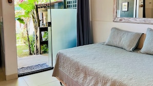 A bedroom with a bed, a large mirror, and a sliding glass door leading to a balcony with plants. - Tatu Do Bem Hospedagem (Serra)