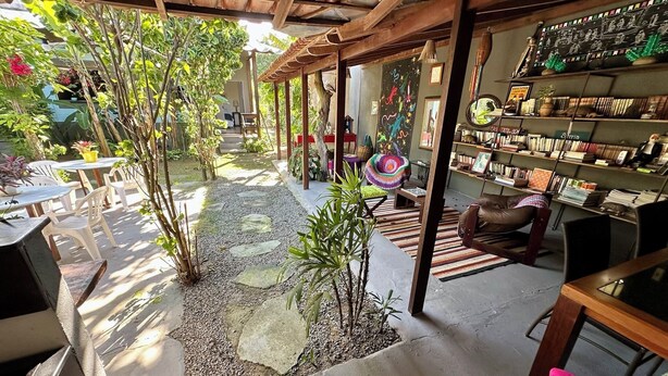 A cozy indoor garden with a stone pathway, wooden furniture, and a bookshelf filled with books. - Tatu Do Bem Hospedagem (Serra)