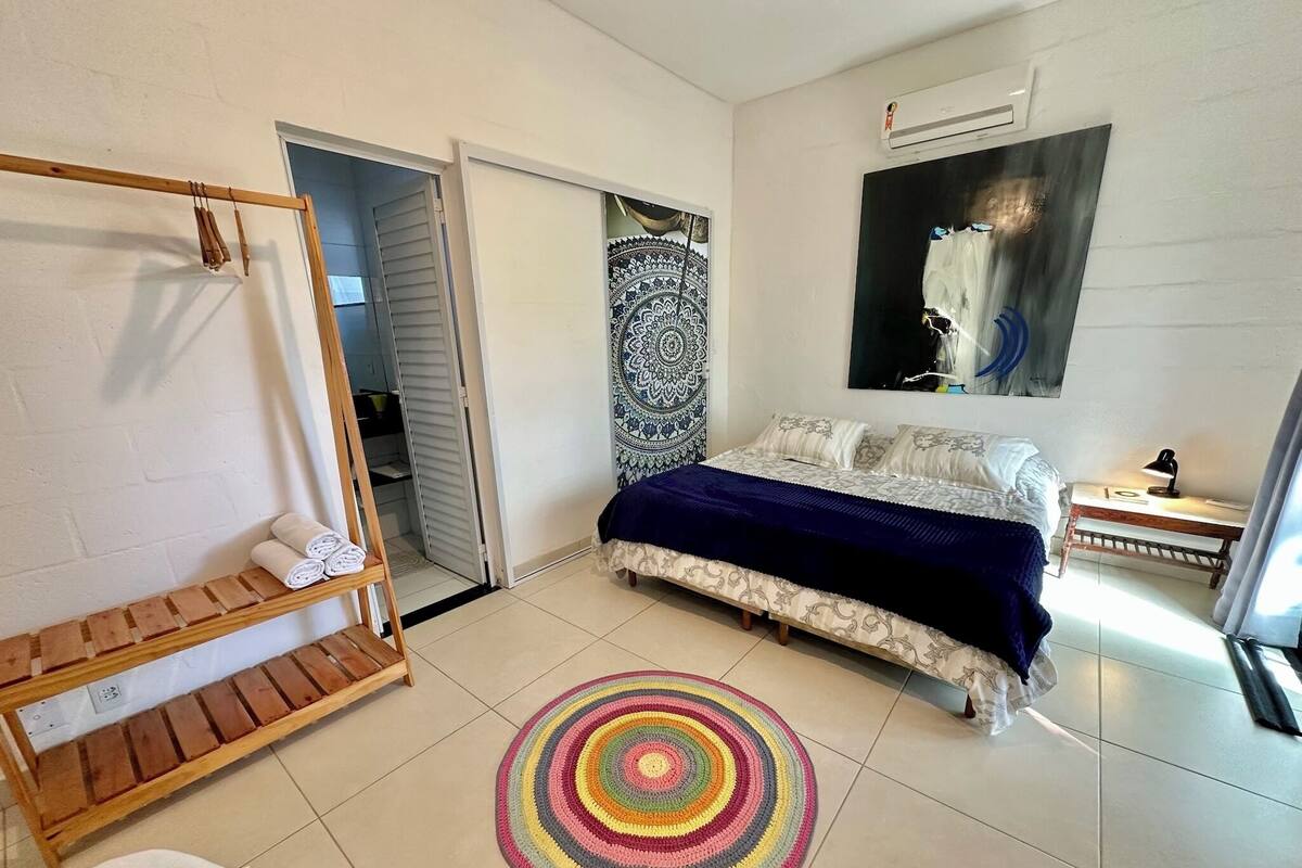 Un dormitorio con una cama, un tapete circular de colores, un banco de madera, un armario y un cuadro en la pared.