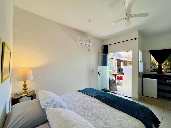 Une chambre d’hôtel avec un lit, un bureau avec une lampe, un ventilateur de plafond et une vue sur l’extérieur.