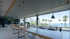 A modern dining area with large windows, white chairs, and hanging pendant lights.