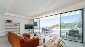 A modern living room with a sofa, chairs, a TV, and a dining area with a view of a cityscape.