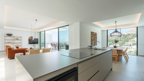 A modern kitchen with a large island, dining area with a view, and a living space with a sofa and chairs.