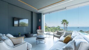 A modern living room with a large window overlooking a beach, furnished with sofas and a coffee table.