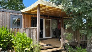 Eine Holzterrasse mit überdachtem Patio, einem Eingang mit Glastüren und einer kleinen Sitzgruppe mit Tisch und Stühlen.