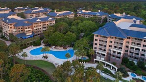 A resort with multiple buildings, a central swimming pool, and surrounding greenery.