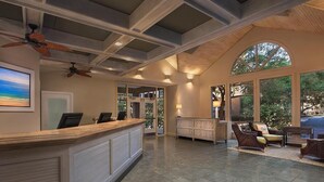 A reception area with a wooden reception desk, seating area with wicker furniture, and large windows offering a view of the outdoors.