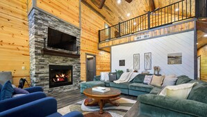 A cozy living room with a stone fireplace, a green sofa set, and a wooden ceiling.