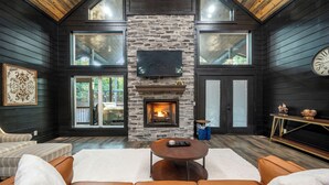 A cozy living room with a stone fireplace, leather sofas, and a large TV mounted on the wall. - NEW Sexy Red Room - Outdoor Movie - Spa - Sauna (Broken Bow)