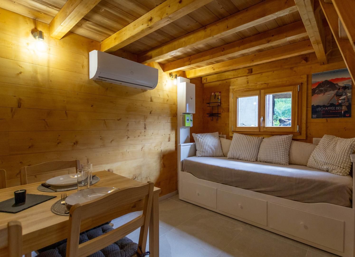 A cozy cabin with a wooden interior, a bed with pillows, a table with plates and glasses, and an air conditioning unit.