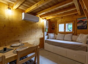 A cozy cabin with a wooden interior, a bed with pillows, a table with plates and glasses, and an air conditioning unit.