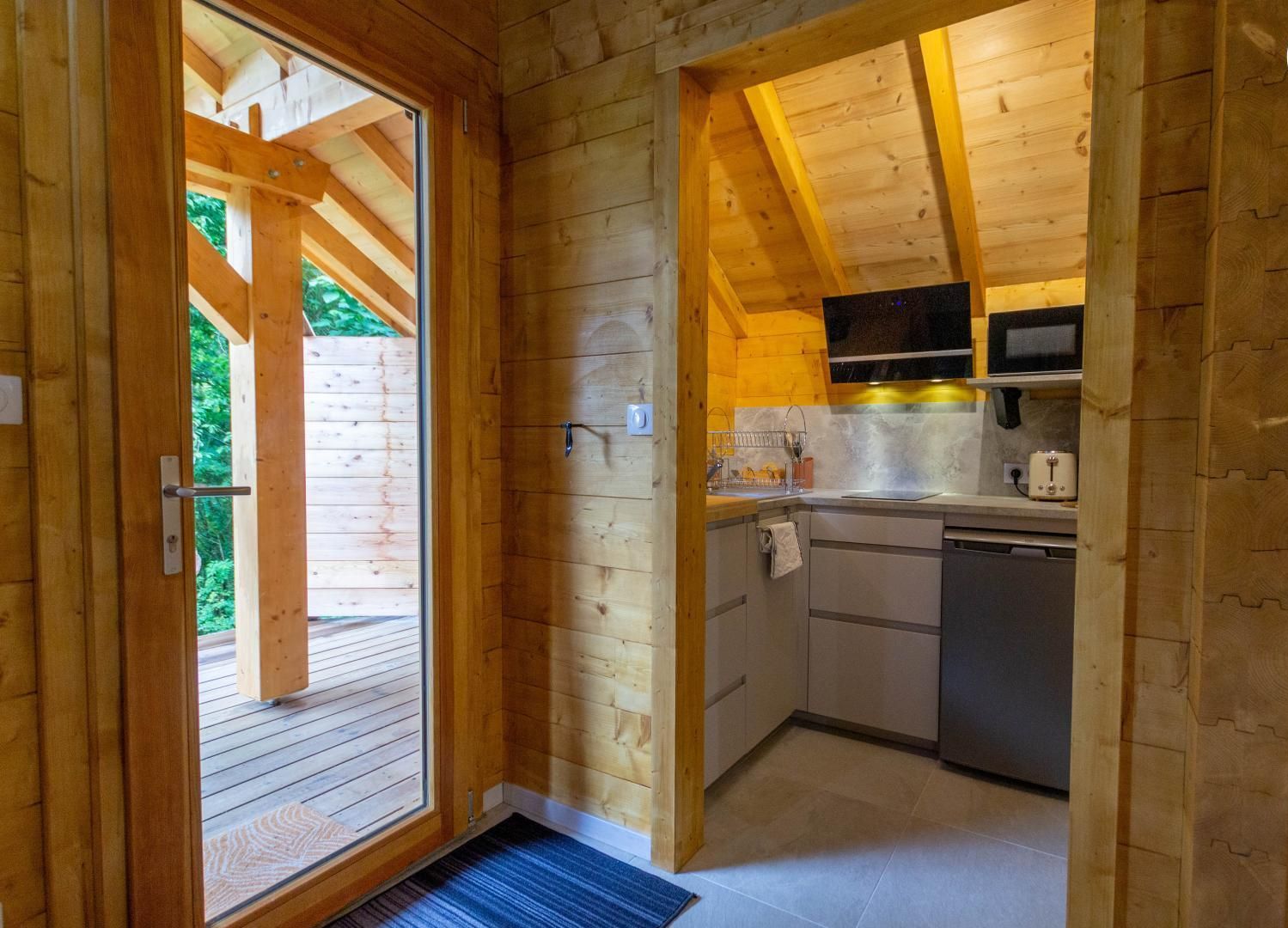 Interior de una cabaña de madera con área de cocina, que incluye microondas, fregadero y armarios.