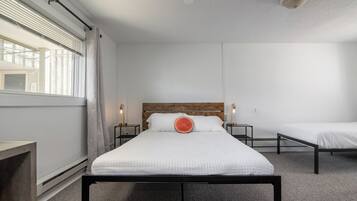 A bedroom with a large bed, two bedside tables, a wooden headboard, a window with blinds, and a ceiling light.