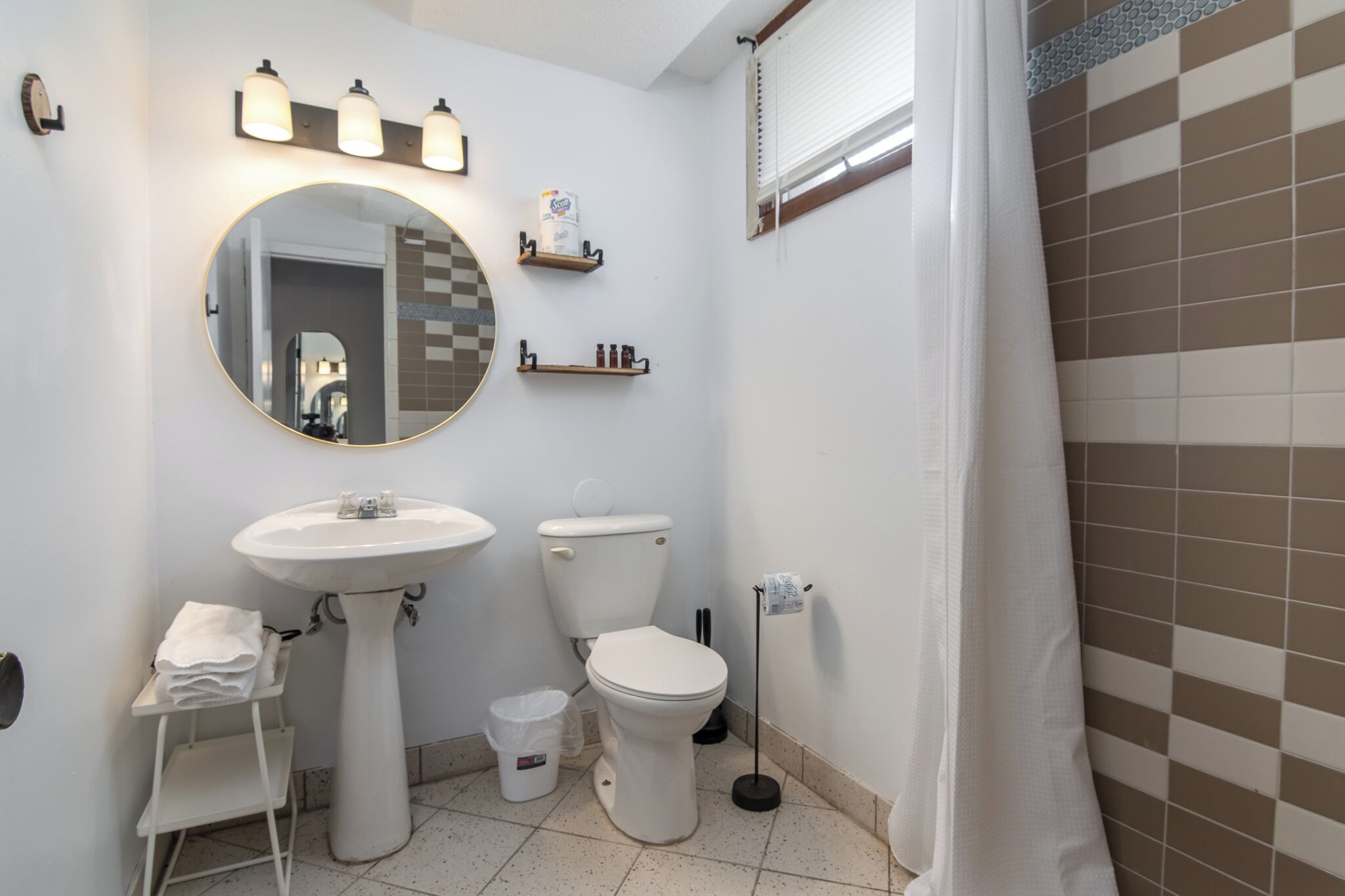 Ein Badezimmer mit einem Standwaschbecken, einem runden Spiegel, einer Toilette und einer Duschvorhang.