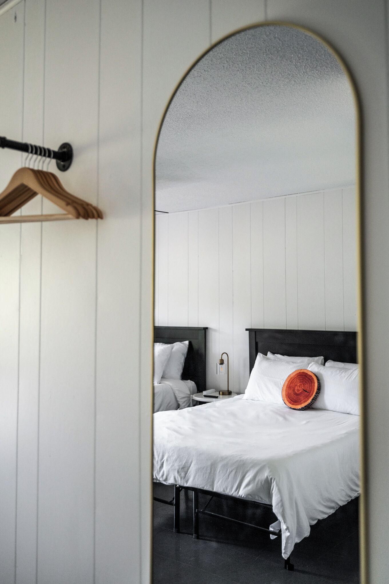 A bedroom with a bed, a bedside table, a hanging rack, and a mirror reflecting the room.