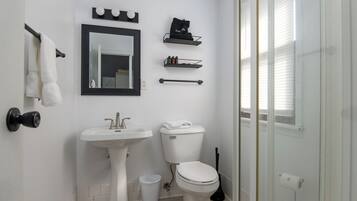 Un baño con lavamanos, inodoro, espejo, toallero y estantes para almacenamiento.