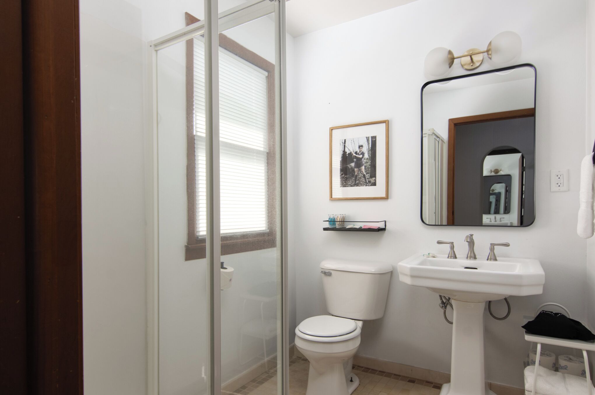 Un baño con inodoro, lavabo, cabina de ducha con mampara de vidrio y una foto enmarcada en la pared.