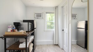 A compact kitchen with a microwave, stove, and refrigerator, a small window with curtains, and a wooden shelf with towels. - Lumberjill Lodge (Balsam Lake)
