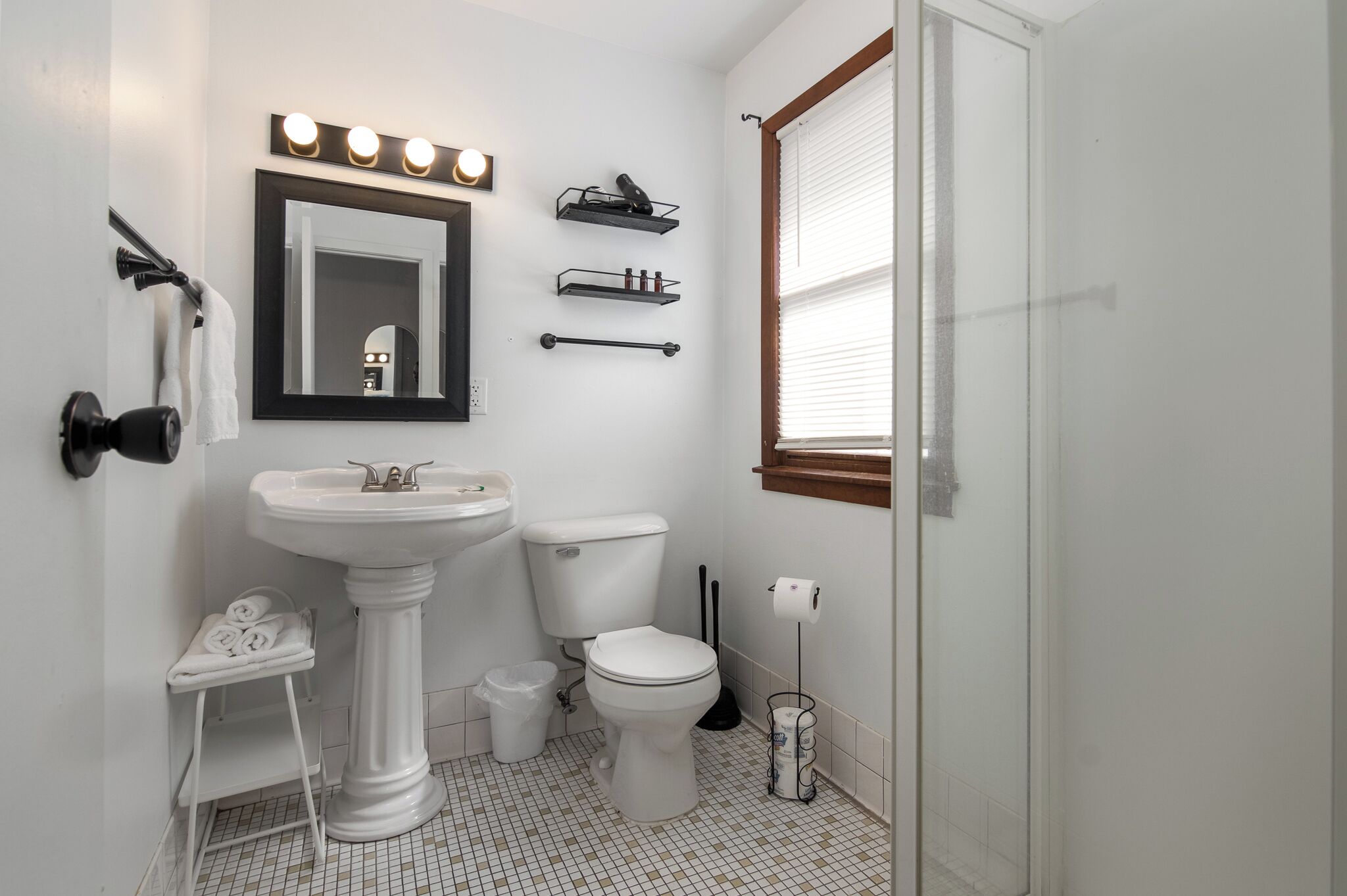 A bathroom with a pedestal sink, toilet, and vanity mirror.