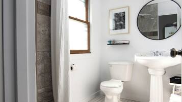 A bathroom with a toilet, sink, mirror, and a framed picture on the wall.