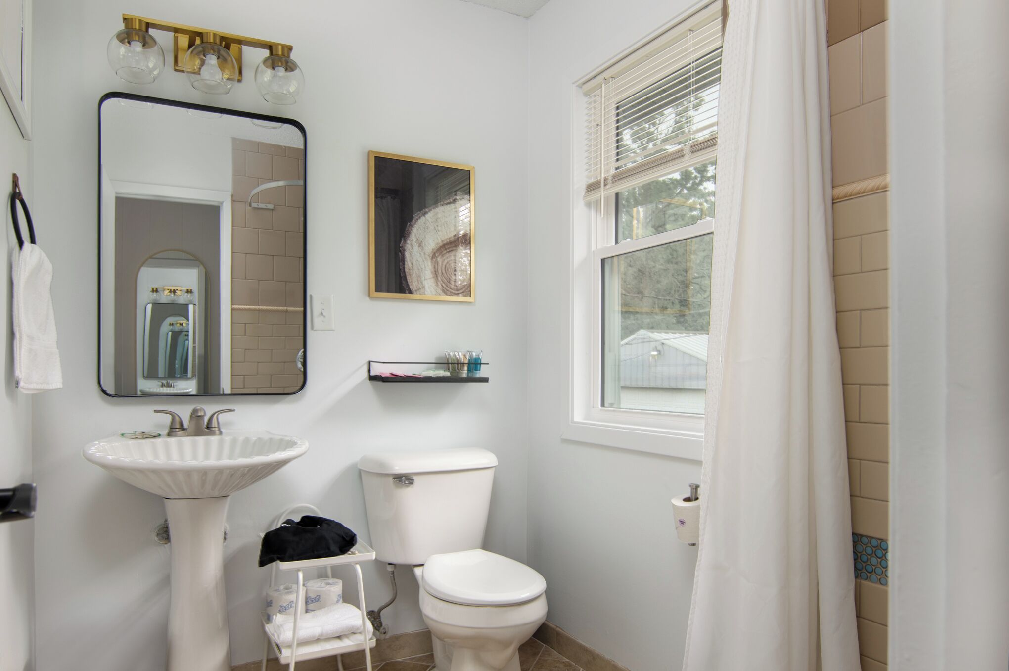 Une salle de bain avec un lavabo blanc, des toilettes et une fenêtre avec un rideau.