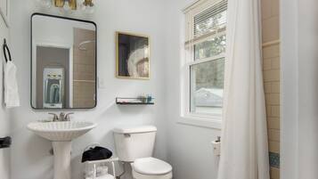 Une salle de bain avec un lavabo blanc, des toilettes et une fenêtre avec un rideau.