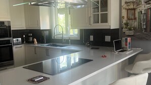 Een moderne keuken met een centraal eiland, roestvrijstalen apparatuur en witte barkrukken.