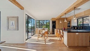 Een moderne keuken met houten kasten, een groot kookeiland, hanglampen en een eethoek met tafel en stoelen.