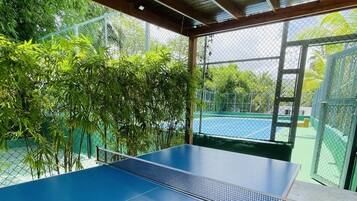 An indoor ping pong table with a net, surrounded by a chain-link fence and bamboo plants.