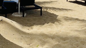 Een strand met ligbedden, een grote parasol en een kajak in het zand.