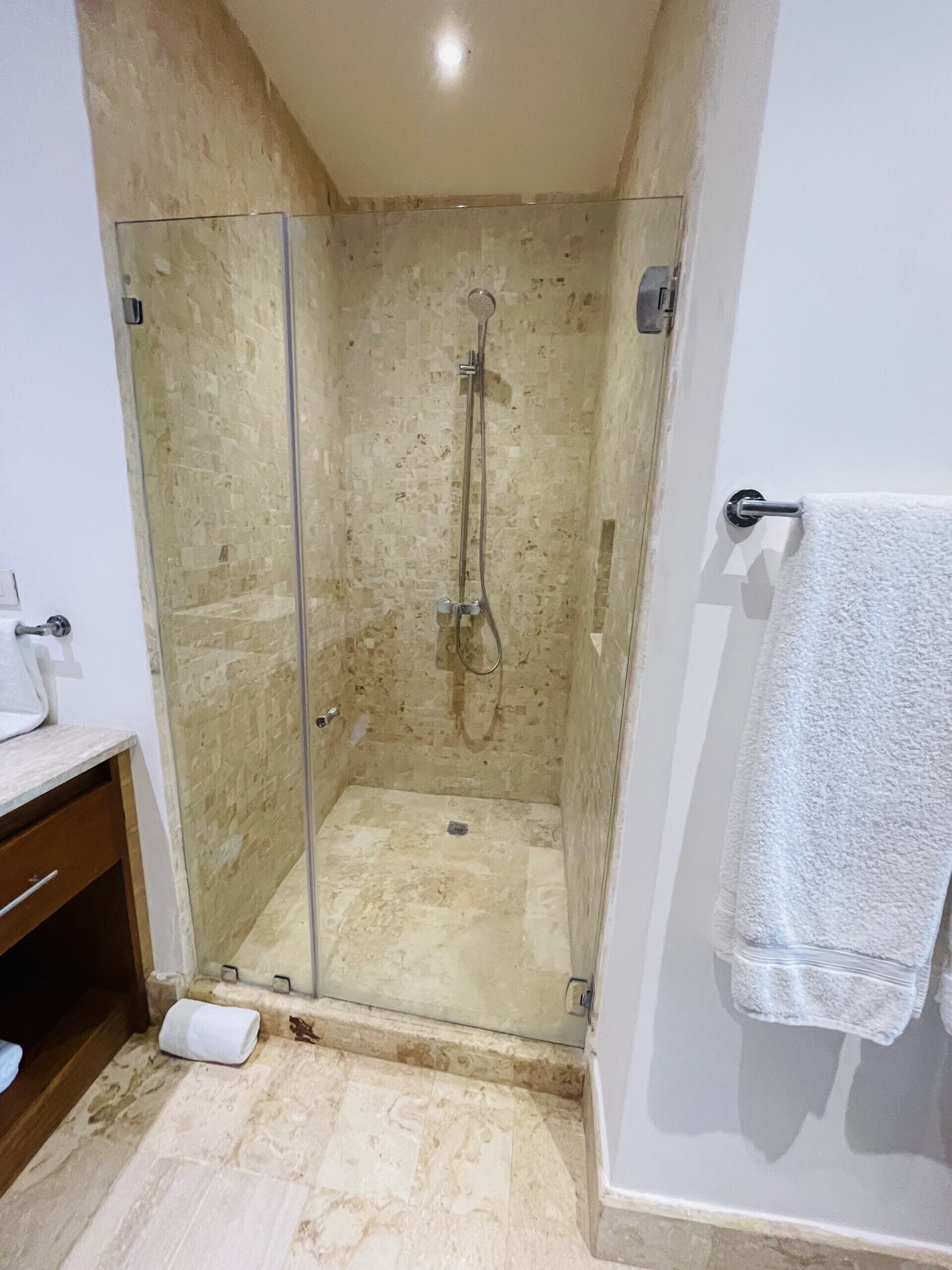 A glass-enclosed shower with a handheld showerhead and a wall-mounted faucet.