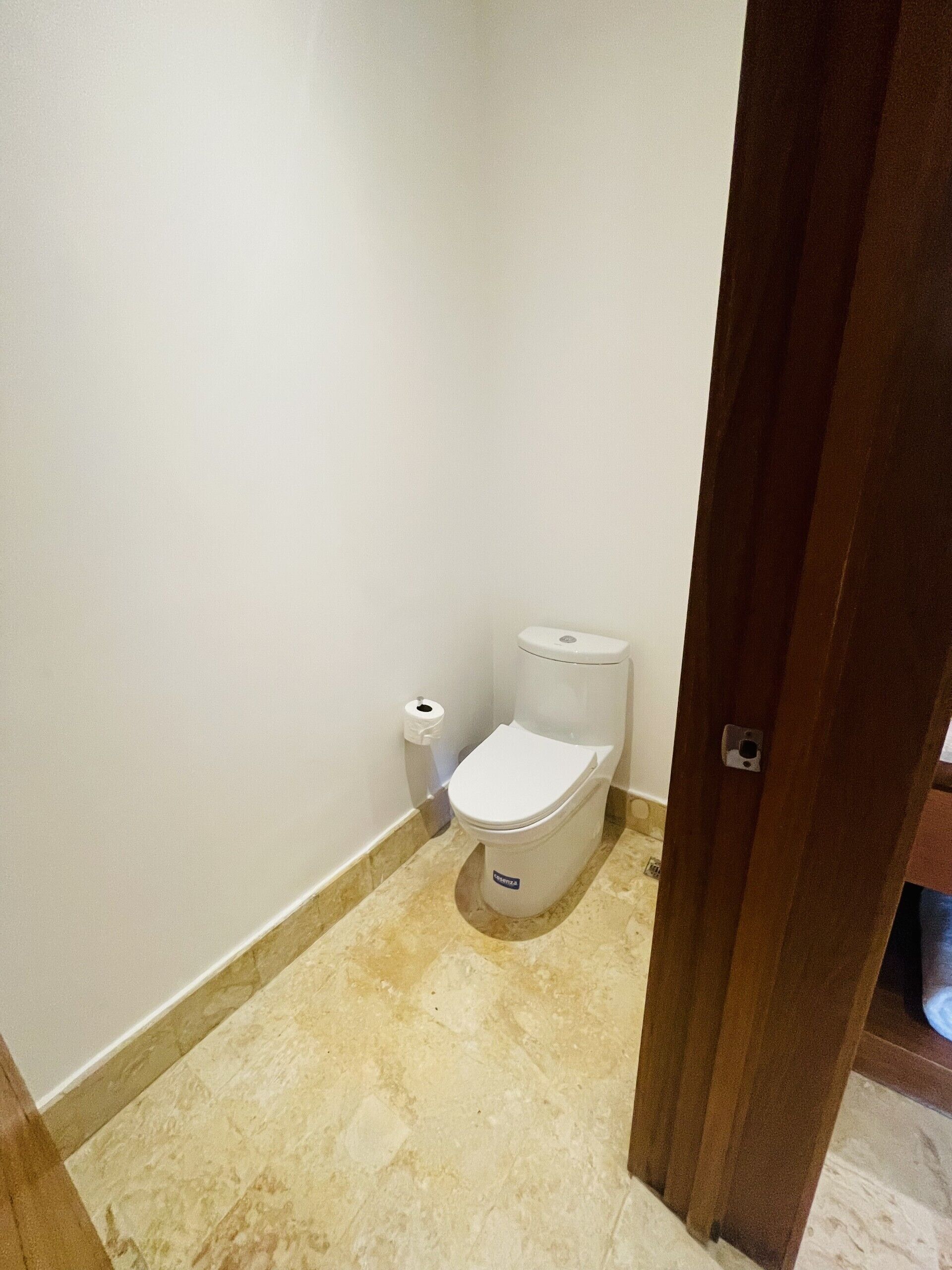 Een kleine badkamer met een toilet, een rol toiletpapier en een marmeren vloer.