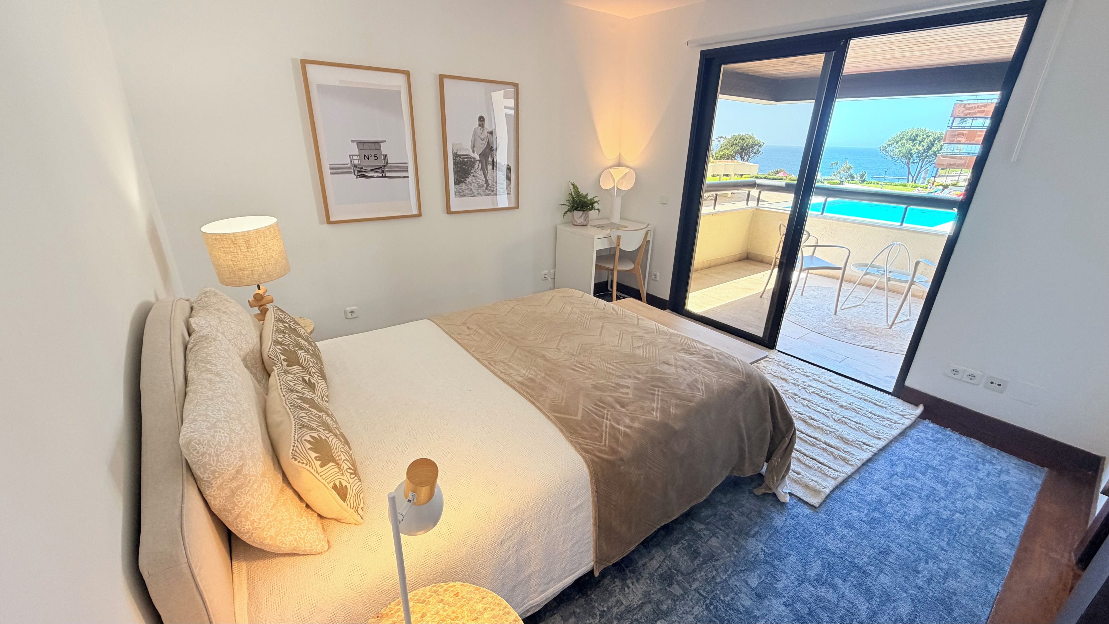 Ein Schlafzimmer mit Bett, Schreibtisch, Stuhl und Blick auf einen Pool durch eine Glastür.