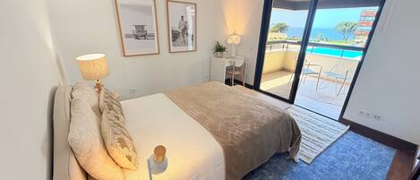 Un dormitorio con cama, escritorio, silla y vista a una piscina a través de una puerta de vidrio.