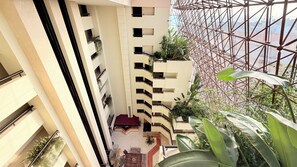 A multi-story building with balconies, a central atrium, and a view of the cityscape through a glass structure.