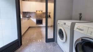 A compact kitchen with white cabinets, a built-in oven, and a washing machine. - Hygge Living Lisbon-Belém Long Stay (Lisboa)