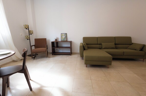 A living room with a brown chair, a green sofa, a small wooden table, and a floor lamp.