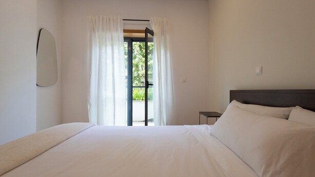 A bedroom with a bed, a nightstand, and a window with curtains. - Hygge Living Lisbon-Belém Long Stay (Lisboa)