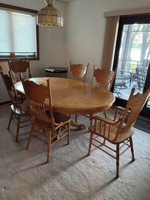 A dining room with a round wooden table and matching chairs, a chandelier, and a view through a glass door to an outdoor patio.