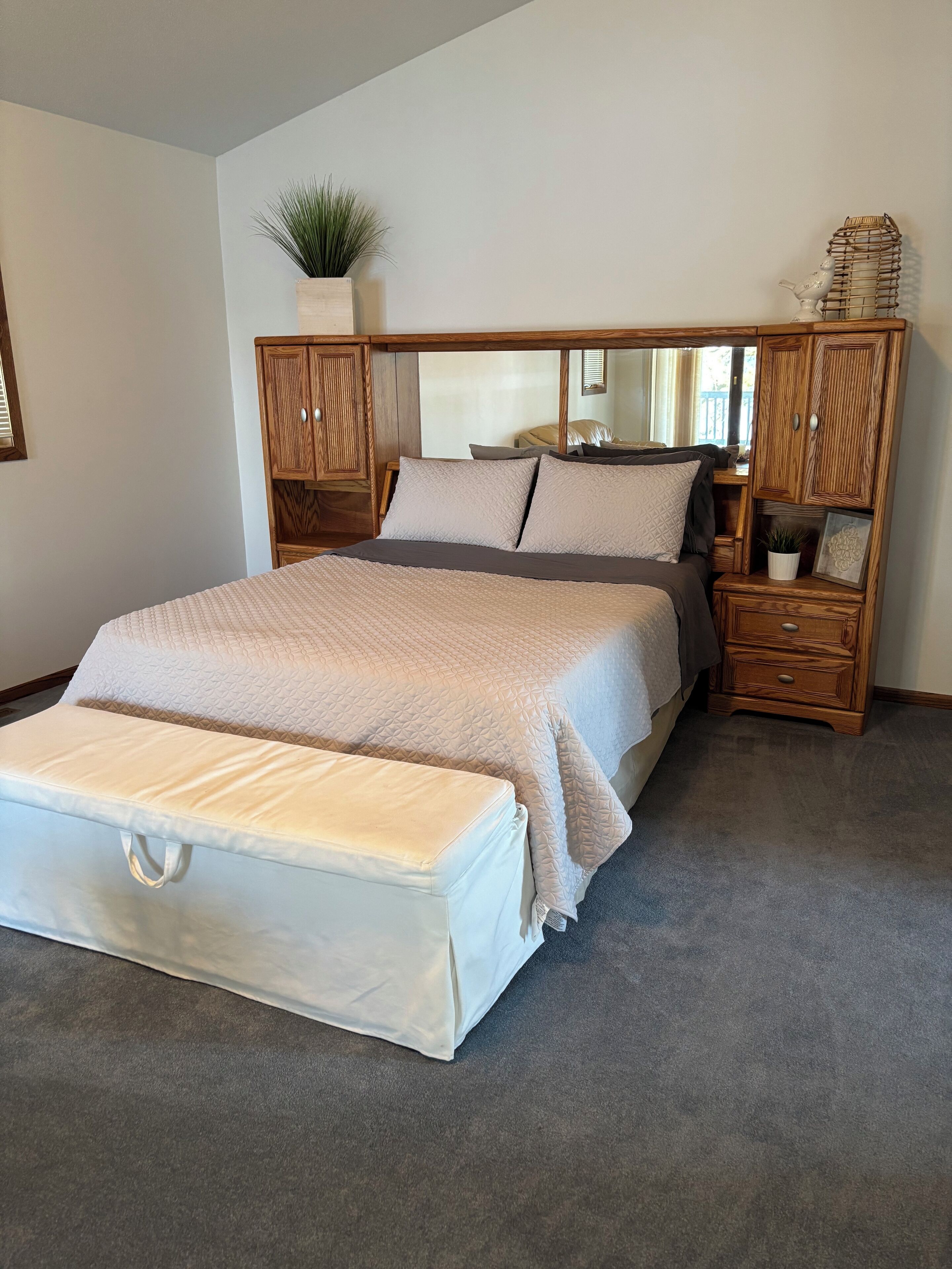 A bedroom with a large bed, a nightstand, a dresser, and a mirror.