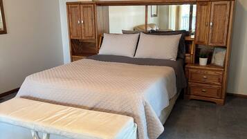 A bedroom with a large bed, a nightstand, a dresser, and a mirror.