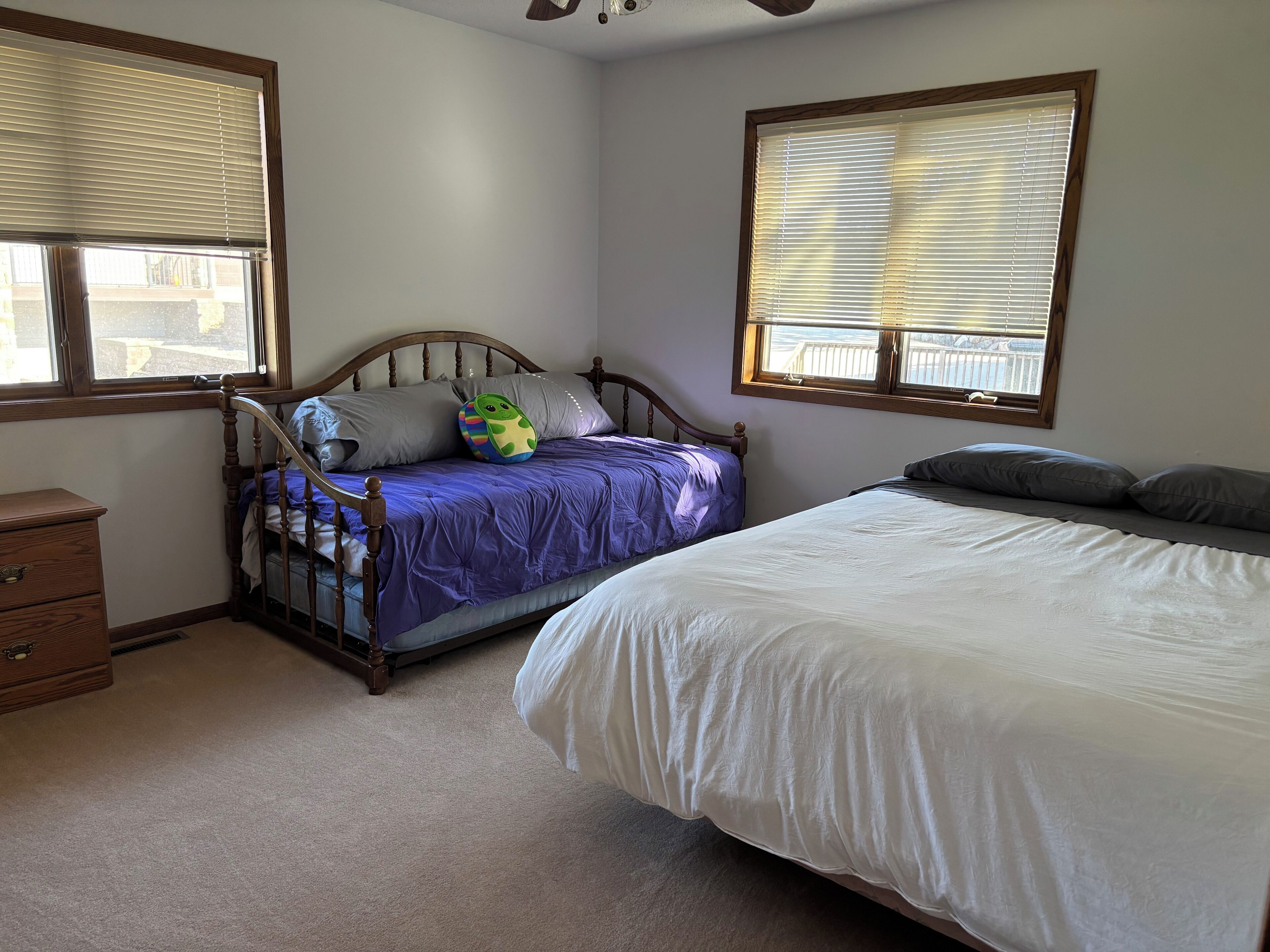 A bedroom with two beds, a wooden headboard, a dresser, and windows with blinds.