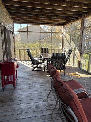 A covered outdoor area with a wooden deck, a red cart, and seating with cushions.