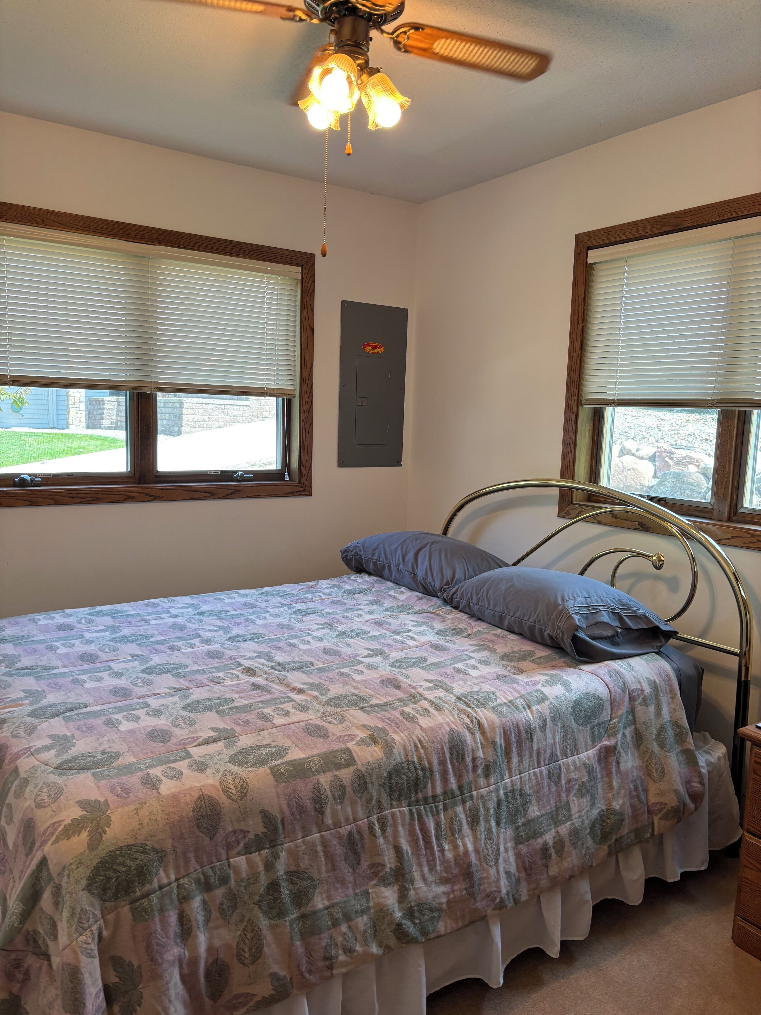 A bedroom with a bed, a ceiling fan, and two windows with blinds.