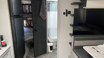 Een ruimtelijk ingerichte camper met een kitchenette, een bed, een badkamer en een televisie.