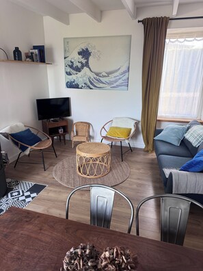 A living room with a television, wicker chairs, a sofa, a dining table, and a Japanese art print on the wall.