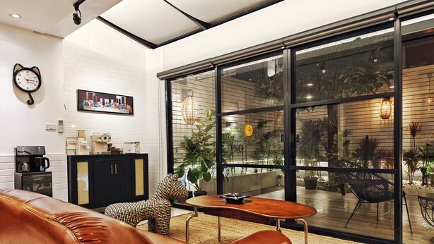 A modern living room with a leather sofa, a small coffee table, and a black cabinet. There is a large window with a view of a garden.